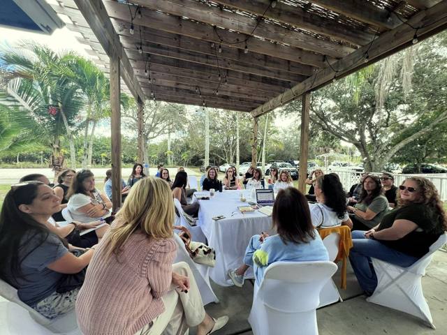 A circle of women learning together around a table under the open-sided pergola