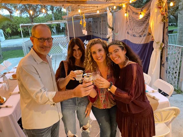 Friends raising a toast at the long tables in the sukkah at Liumi