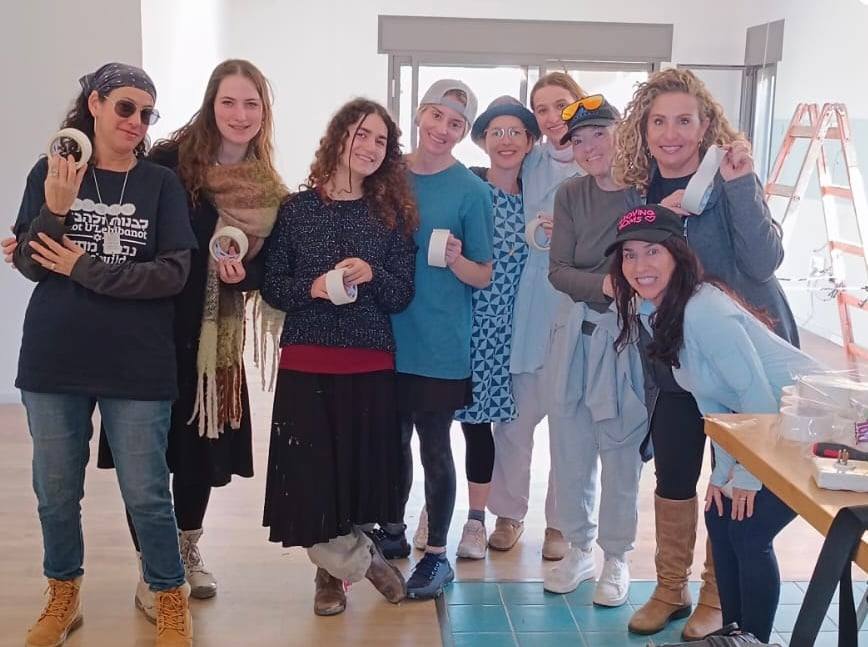 The Livnot volunteer team, nine women holding rolls of painter's tape in a freshly prepared room on the kibbutz
