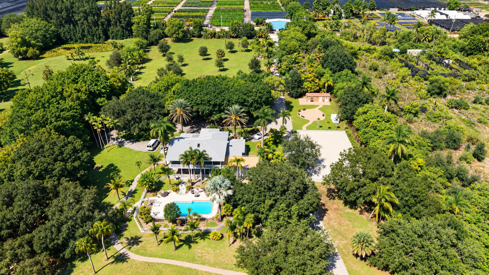The Liumi property from the air: the retreat house and pool at the centre, open field and fruit trees to the left, the cabin and its bench circle to the right, and woodland around the edges.